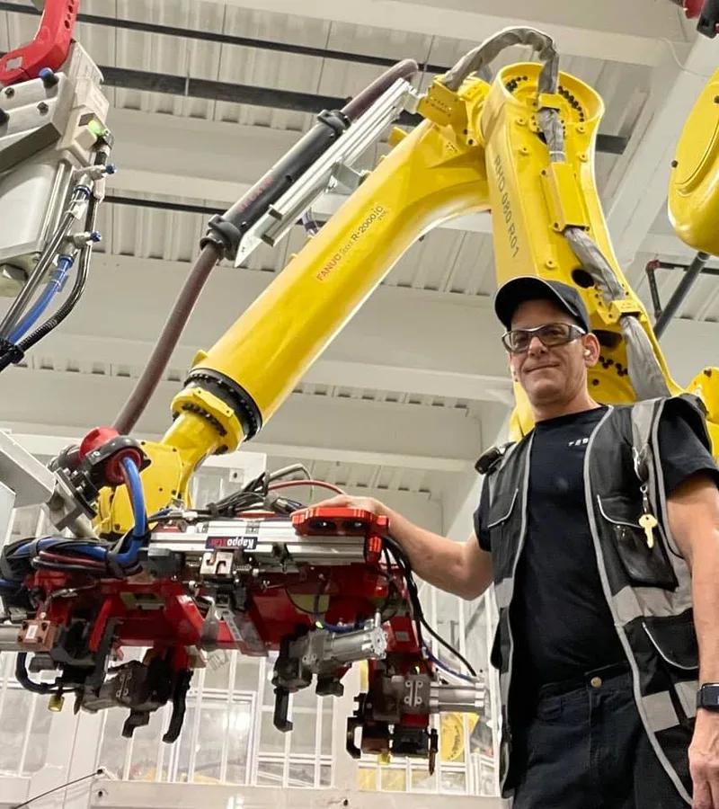 Murphy standing next to a FANUC R-2000 robot arm at Tesla Gigafactory